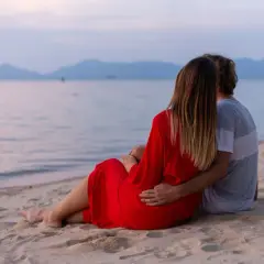 Para dla dwojga siedzi na plaży, patrząc na morze. Idealne fajne miejsce nad morzem dla dwojga, by podziwiać zachód słońca.