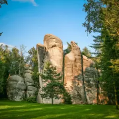 Skalne miasto w Czechach, z imponującymi piaskowcowymi formacjami skalnymi otoczonymi zielenią i drzewami.