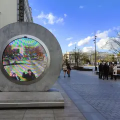 Lublin nietypowe atrakcje: okrągła instalacja z ekranem wyświetlającym barwny obraz miasta i ludzi. Spacer po placu w słoneczny dzień.