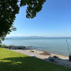 Słoneczny dzień nad Jeziorem Bodeńskim. Plaże z kamykami, łodzie i zielona trawa zapraszają do relaksu.