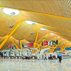 Nowoczesna architektura lotniska Madryt Barajas z żółtymi podporami i drewnianym sufitem.