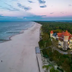 Zachód słońca nad morzem, piaszczysta plaża i zabytkowy budynek z wieżą w Łebie.