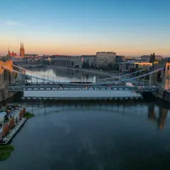 Most wiszący nad Odrą rzeką jak płynie, z widokiem na miasto i katedrę.