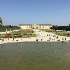 Piękny pałac Schönbrunn i jego ogrody, symbol wiedeńskiej historii. Ludzie spacerują pośród kwiatów i przy stawie.