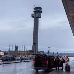 Wieża kontrolna na oslo lotnisko. Samochody czekają na pasażerów, a bagaże są wyładowywane.
