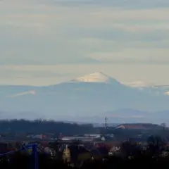 Widok na Śnieżkę i Karkonosze z Wrocławia. W oddali majaczą ośnieżone szczyty górskie, a na pierwszym planie widać zabudowania miejskie.