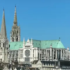 Katedra w Chartres, symbol francuskiej religii, z zielonym dachem i strzelistymi wieżami na tle błękitnego nieba.