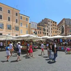 Tętniący życiem targ na Campo di Fiori w Rzymie, z ludźmi spacerującymi między straganami z pamiątkami i jedzeniem.