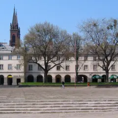 Łódź stare miasto: plac z kamiennymi schodami, arkadowymi budynkami i wieżą kościelną w tle.