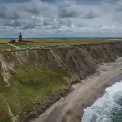 Dania góry: czerwona latarnia morska na klifie, plaża, morze i paralotniarz w oddali.