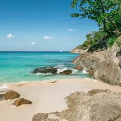 Piękne plaże Phuket z turkusową wodą, piaszczystym brzegiem i skalistym wybrzeżem. Na horyzoncie biała łódź.