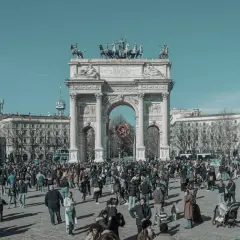 Tłum ludzi na placu przed imponującym łukiem triumfalnym w Mediolanie.