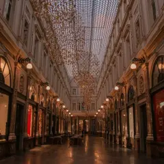 Elegancka galeria handlowa w Brukseli, z rzędem sklepów i kawiarni, ozdobiona złotymi, wiszącymi instalacjami. To urokliwe miejsce, które warto odwiedzić, zwiedzając brukselskie dzielnice.