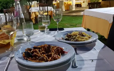 Dwa talerze makaronu z owocami morza, kieliszki wina i chleb na stole w restauracji pod gołym niebem.