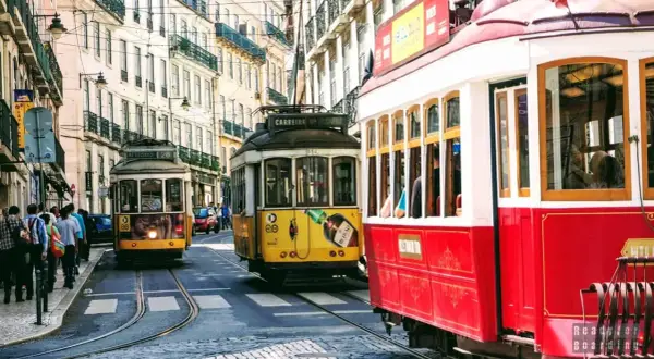 Żółty i czerwony tramwaj w Lizbonie pędzą wąską uliczką między zabytkowymi kamienicami.