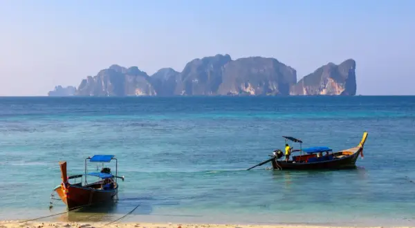 Dwie łodzie dryfują na turkusowej wodzie, w tle majaczą skaliste wyspy. Idealne miejsce na wakacje na wyspach Phuket.