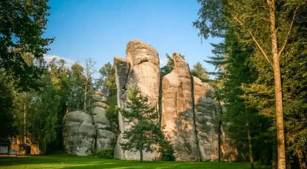 Skalne miasto w Czechach, z imponującymi piaskowcowymi formacjami skalnymi otoczonymi zielenią i drzewami.
