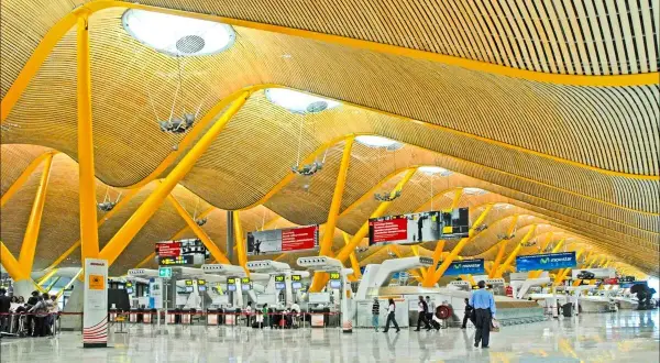 Nowoczesna architektura lotniska Madryt Barajas z żółtymi podporami i drewnianym sufitem.
