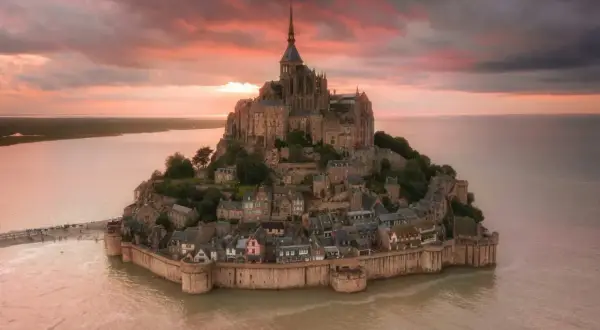Bajkowy zamek na wodzie we Francji, Mont Saint-Michel, otoczony wodą o zachodzie słońca.