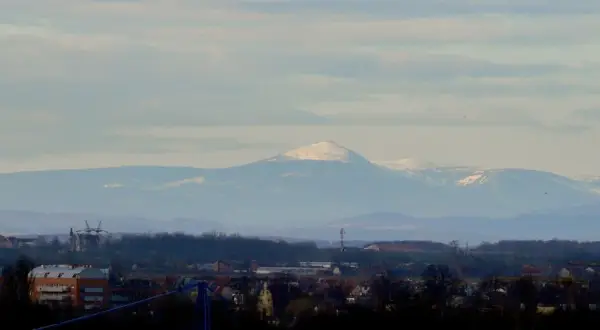 Widok na Śnieżkę i Karkonosze z Wrocławia. W oddali majaczą ośnieżone szczyty górskie, a na pierwszym planie widać zabudowania miejskie.