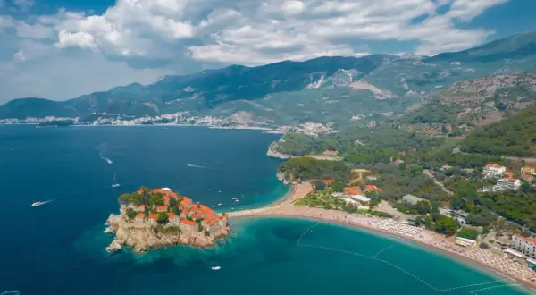 Sveti Stefan, Czarnogóra na co uważać? Urokliwa wyspa z czerwonymi dachami, połączona z lądem piaszczystą mierzeją, otoczona turkusowym morzem i zielonymi wzgórzami.