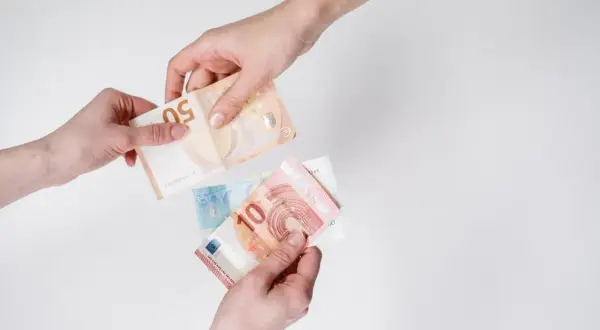 Dwie ręce przekazują sobie banknoty euro. To popularna waluta we Włoszech, używana do codziennych transakcji.