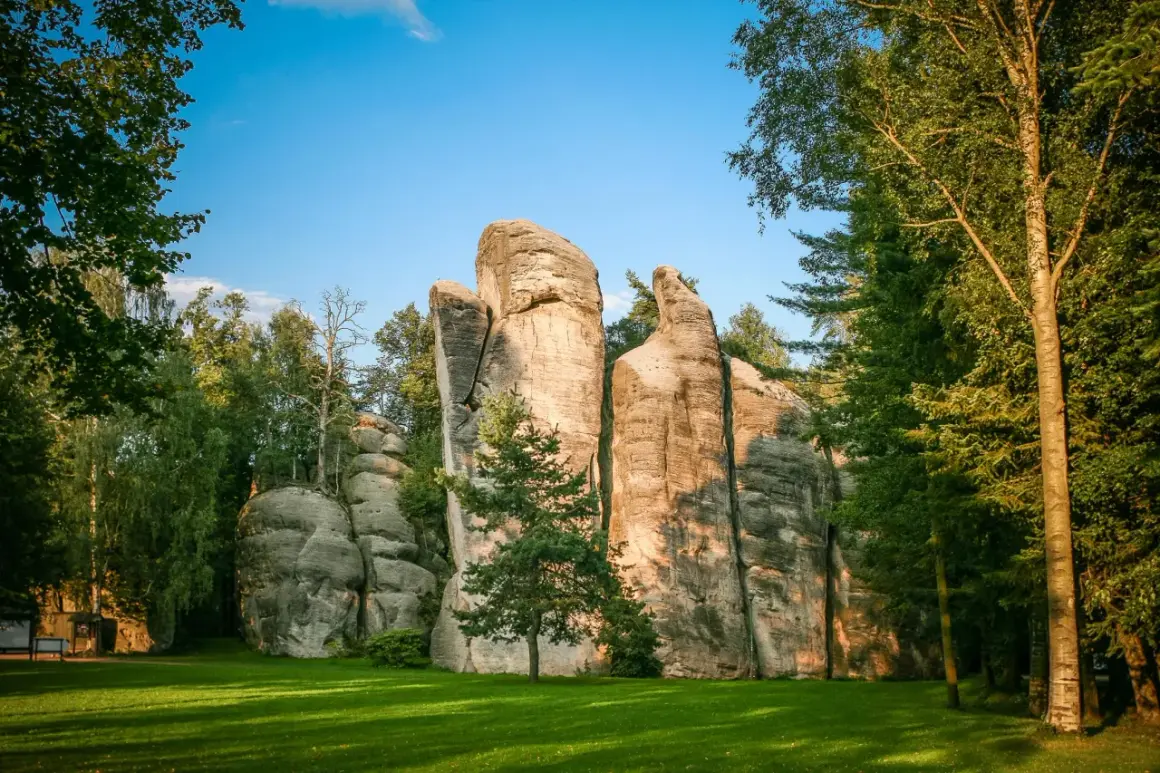 Skalne miasto w Czechach, z imponującymi piaskowcowymi formacjami skalnymi otoczonymi zielenią i drzewami.