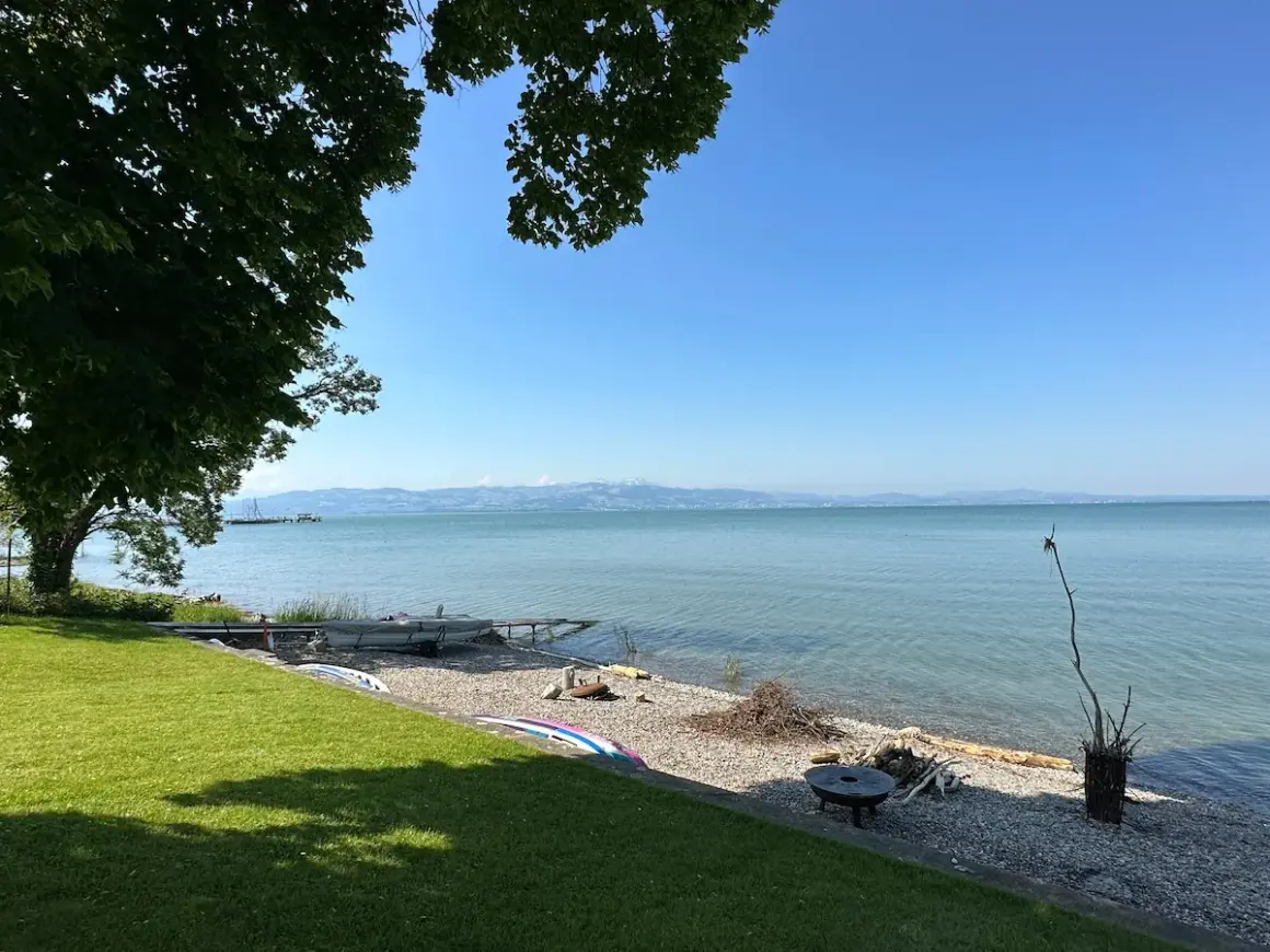 Słoneczny dzień nad Jeziorem Bodeńskim. Plaże z kamykami, łodzie i zielona trawa zapraszają do relaksu.