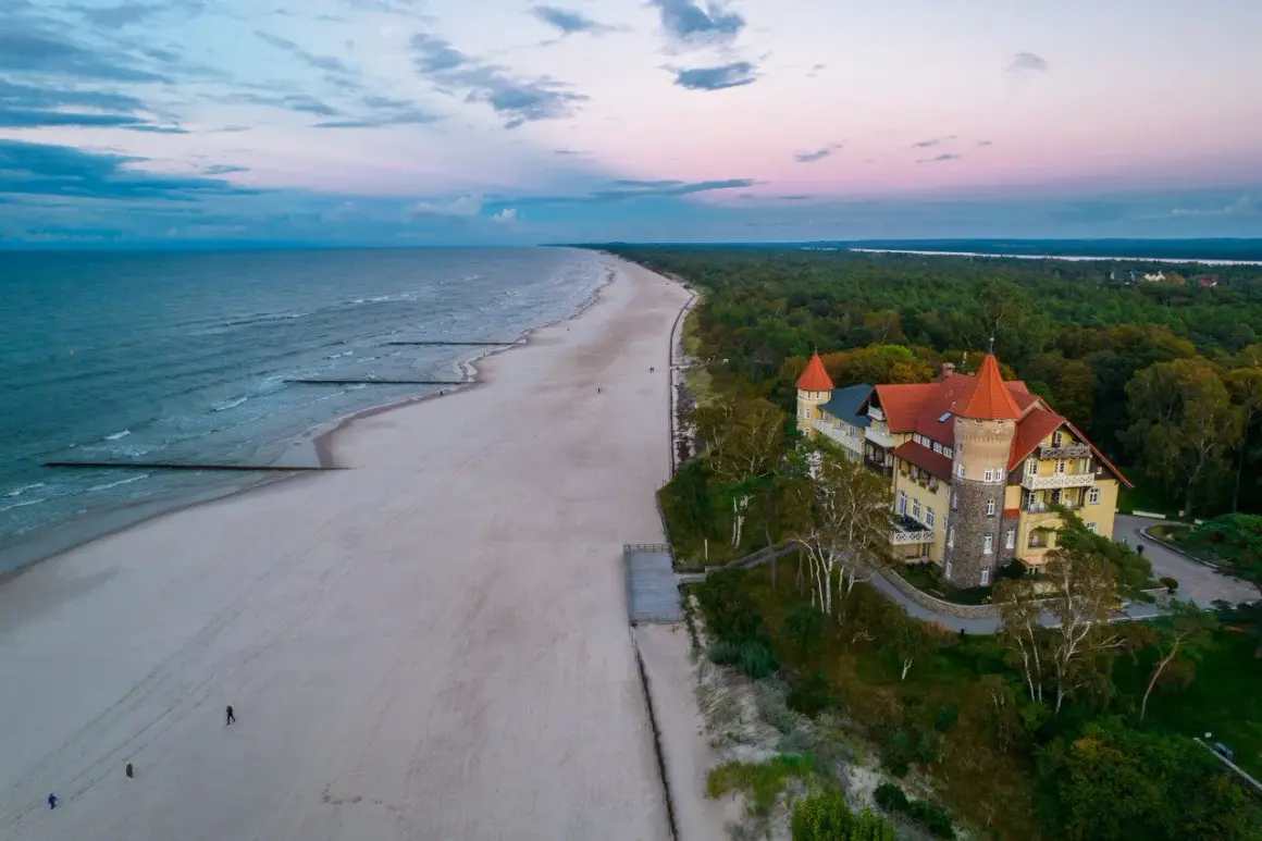 Zachód słońca nad morzem, piaszczysta plaża i zabytkowy budynek z wieżą w Łebie.
