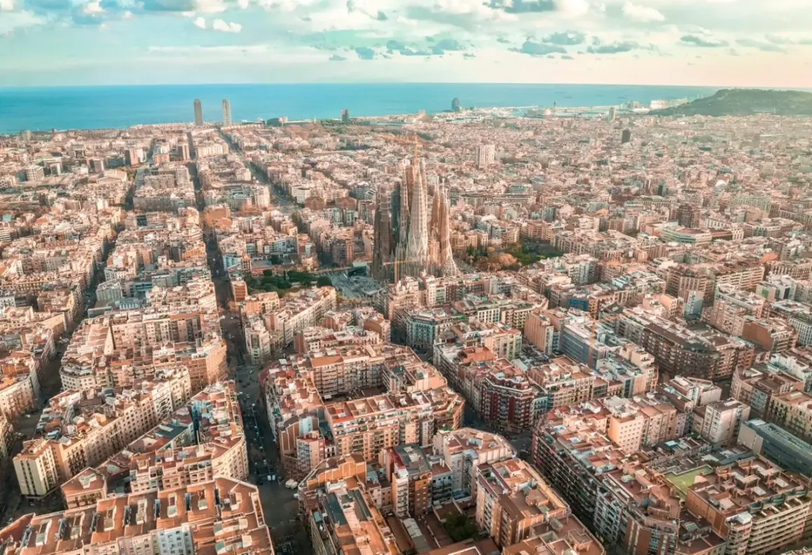 Widok z lotu ptaka na Eixample w Barcelonie, z Sagradą Familią górującą nad miastem i morzem w tle.