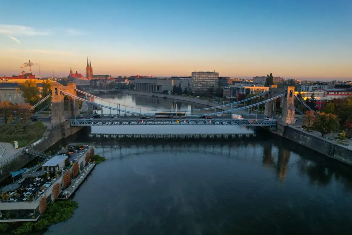 Most wiszący nad Odrą rzeką jak płynie, z widokiem na miasto i katedrę.