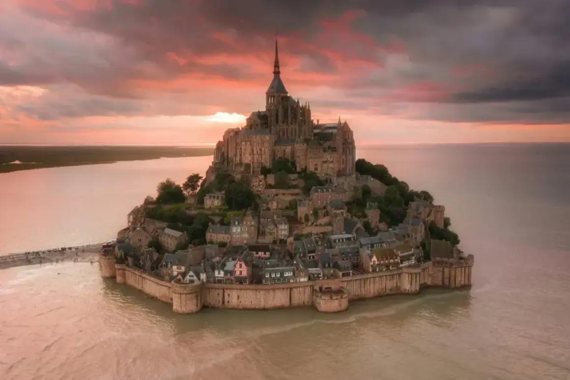 Bajkowy zamek na wodzie we Francji, Mont Saint-Michel, otoczony wodą o zachodzie słońca.
