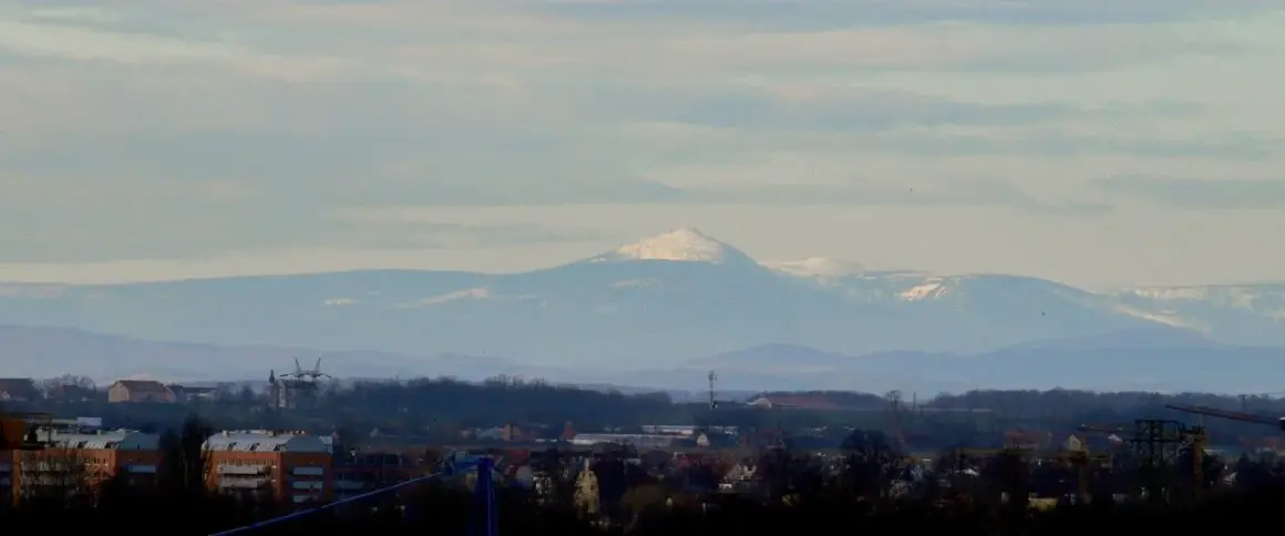 Widok na Śnieżkę i Karkonosze z Wrocławia. W oddali majaczą ośnieżone szczyty górskie, a na pierwszym planie widać zabudowania miejskie.