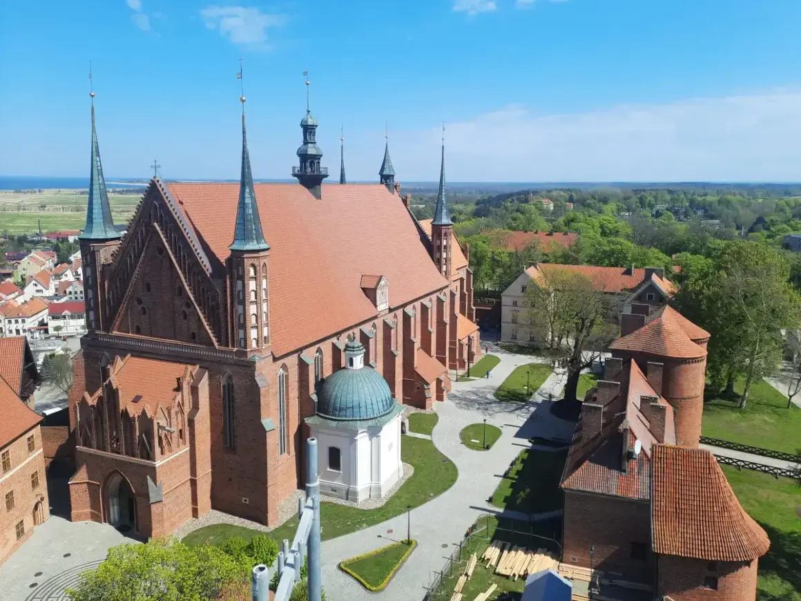 Widok z góry na Frombork zamek i katedrę. Czerwona cegła, zielone dachy i błękitne niebo tworzą malowniczy krajobraz.