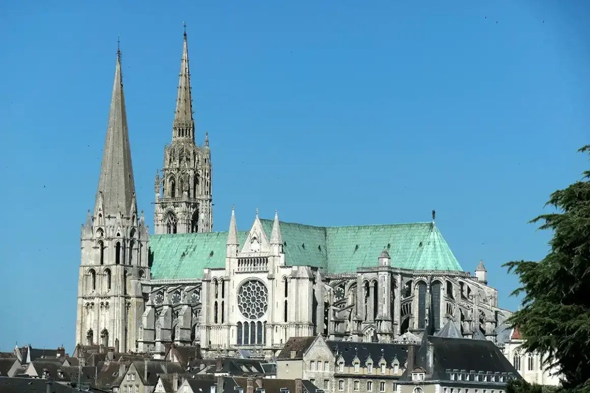 Katedra w Chartres, symbol francuskiej religii, z zielonym dachem i strzelistymi wieżami na tle błękitnego nieba.