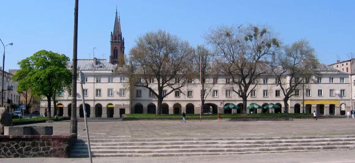 Łódź stare miasto: plac z kamiennymi schodami, arkadowymi budynkami i wieżą kościelną w tle.