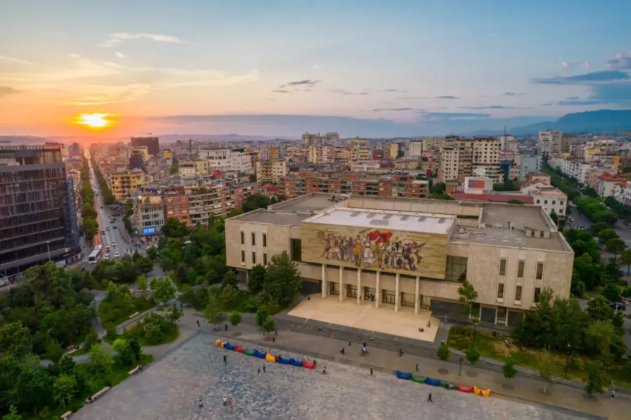 Zachód słońca nad Tirana, stolicą Albanii. Widok na plac z kolorowymi siedziskami i budynek z mozaiką.
