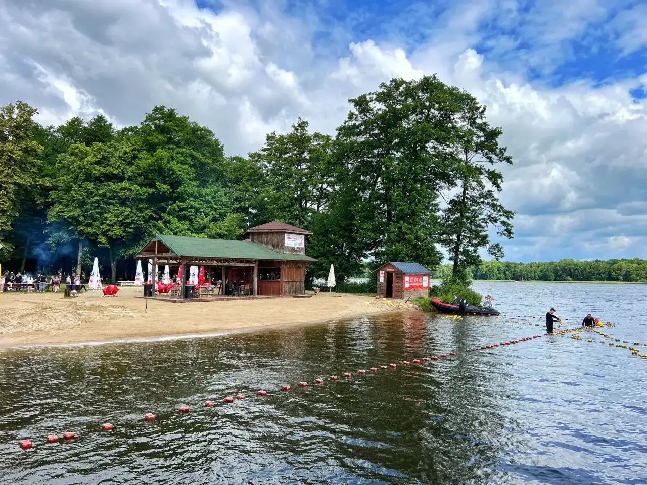 Plaża nad jeziorem w Szczecinku z barem, domkami i ratownikami na wodzie.