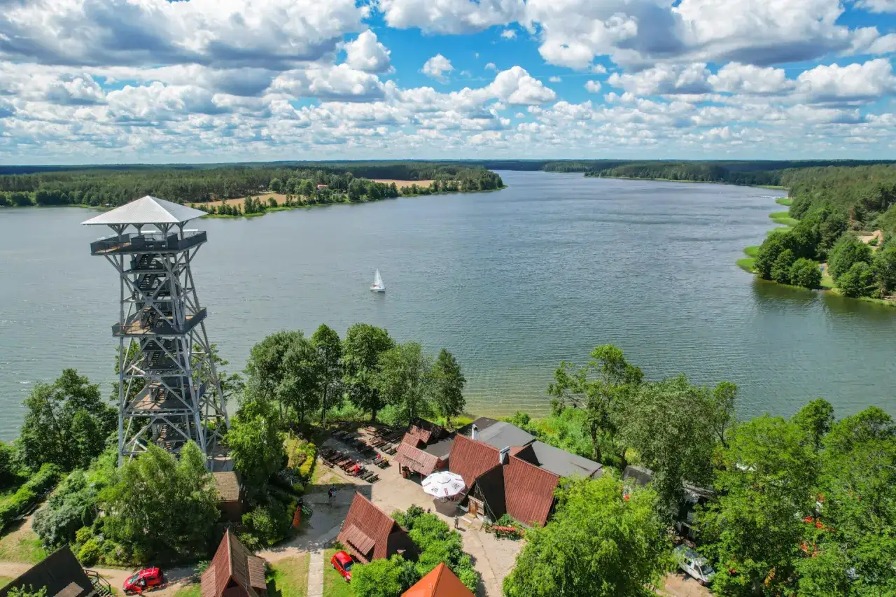 Wieża widokowa nad jeziorem, gdzie są Kaszuby. Żaglówka na wodzie, las i chmury.