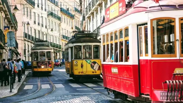 Żółty i czerwony tramwaj w Lizbonie pędzą wąską uliczką między zabytkowymi kamienicami.