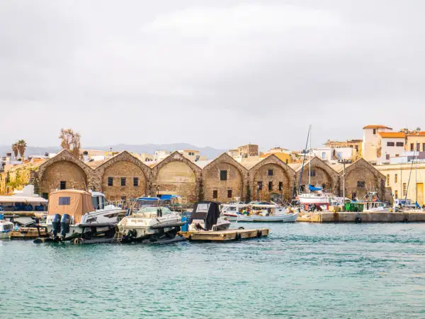 Port w Chanii, Kreta zimą. Łodzie zacumowane przy kamiennych budynkach, w tle góry.