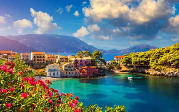 Piękna kefalonia pogoda czerwiec: kolorowe domki nad turkusową zatoką, góry w tle, kwitnące kwiaty na pierwszym planie.