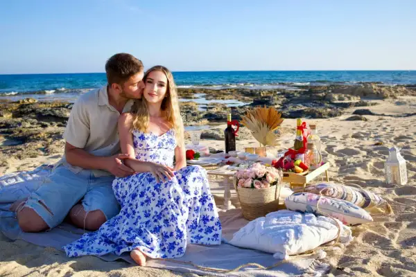 Romantyczny piknik na plaży w Pafos. Para cieszy się chwilą, a piękne widoki i jedzenie zachwycają. Sprawdź pafos ceny, by zaplanować podobny wypad.