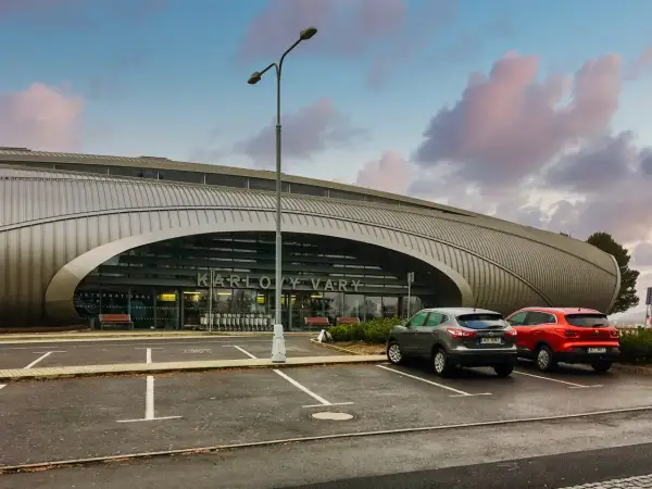 Nowoczesne lotnisko w Czechach, Karlowe Wary, z charakterystyczną, falistą fasadą. Dwa samochody stoją na parkingu przed wejściem.