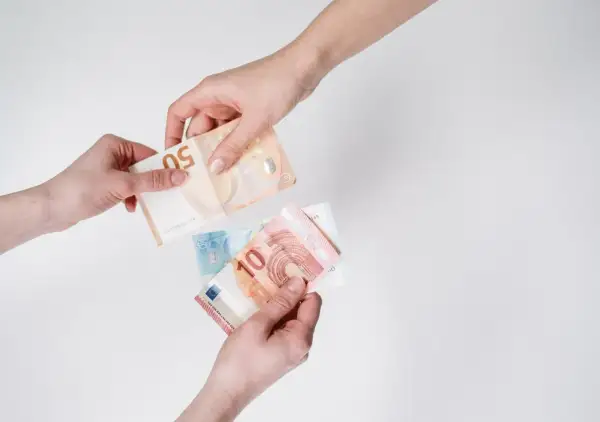 Dwie ręce przekazują sobie banknoty euro. To popularna waluta we Włoszech, używana do codziennych transakcji.